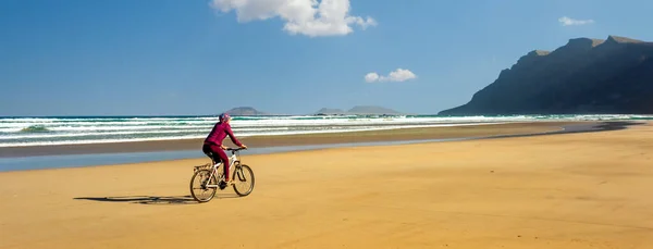 Sportig ung kvinna rida cykel på sandstrand — Stockfoto