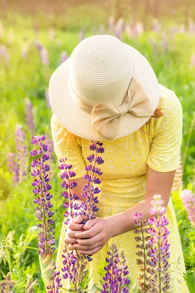 Young happy girl smalls summer flowers on wild field — Stock Photo, Image
