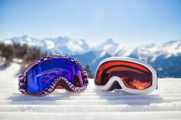 Two ski masks close-up on the snow with mountains in the background