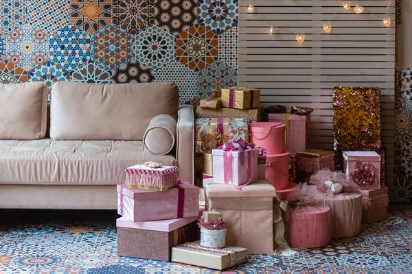 Loft interior. Beige sofa and a lot of gifts in pink colors. Hexagon tile mosaic on the wall and the floor. Festive interior in beige blue and pink color.