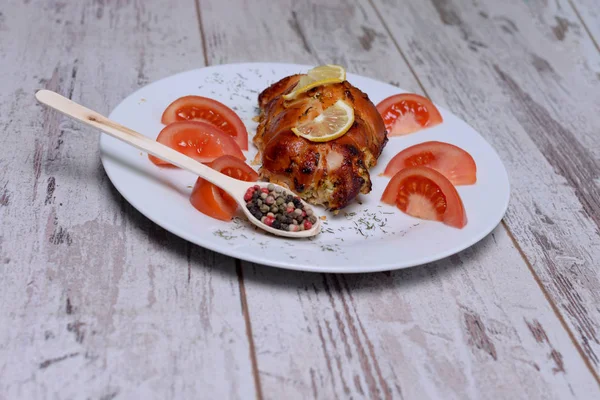 Rollos de pollo al horno con tomate y limón y especias en un plato blanco sobre una mesa de madera blanca — Foto de Stock