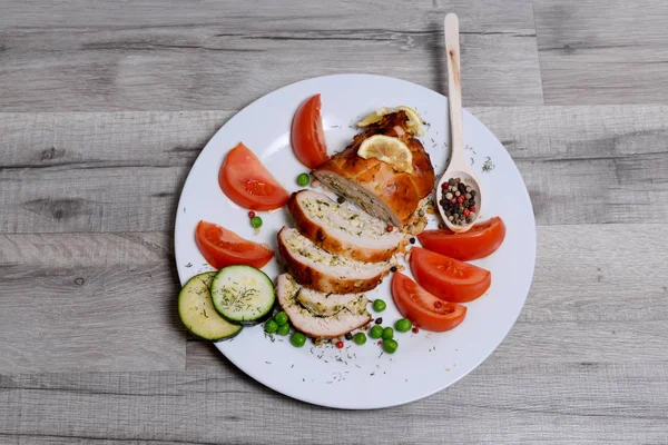 Rollos de pollo al horno con tomate y limón y especias en un plato blanco sobre una mesa de madera blanca — Foto de Stock