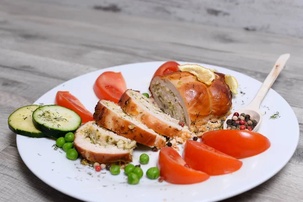Beyaz ahşap bir masa üzerinde beyaz tabakta domates ve limon ve baharat tavuk rulo pişmiş