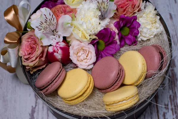 Box mit frischen Blumen und Makronen auf hölzernem Hintergrund — Stockfoto