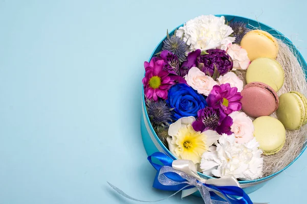 Box with flowers and macaroons on blue background