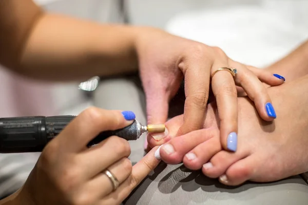 Maestro durante una pedicura. El proceso de pedicuras profesionales. Maestro en mascarilla haciendo pedicura debajo de la lámpara. El concepto de belleza y salud. Foto vertical . —  Fotos de Stock