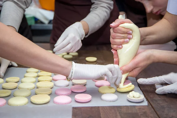 Concepto de cocción, comida y horneado - chef con bolsa de confitería que exprime el relleno de crema a las cáscaras de macarrones en la pastelería — Foto de Stock