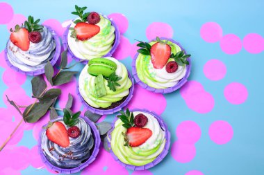 Krem şantili kekler çikolatalı gofret, çilek, mavi arka planda badem kurabiyesi. Menü ya da şekerleme kataloğu için resim. Metin için yeri var. Pembe konfetilerle süslenmiş.