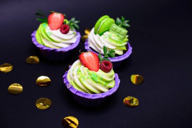 Krem şantili kapkekler çikolatalı gofret, çilek, siyah arka planda badem kurabiyesi. Menü ya da şekerleme kataloğu için resim. metin için boşluk ile