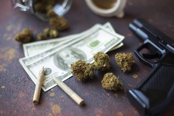Black gun, marijuana cones and dollar bills on a dark table