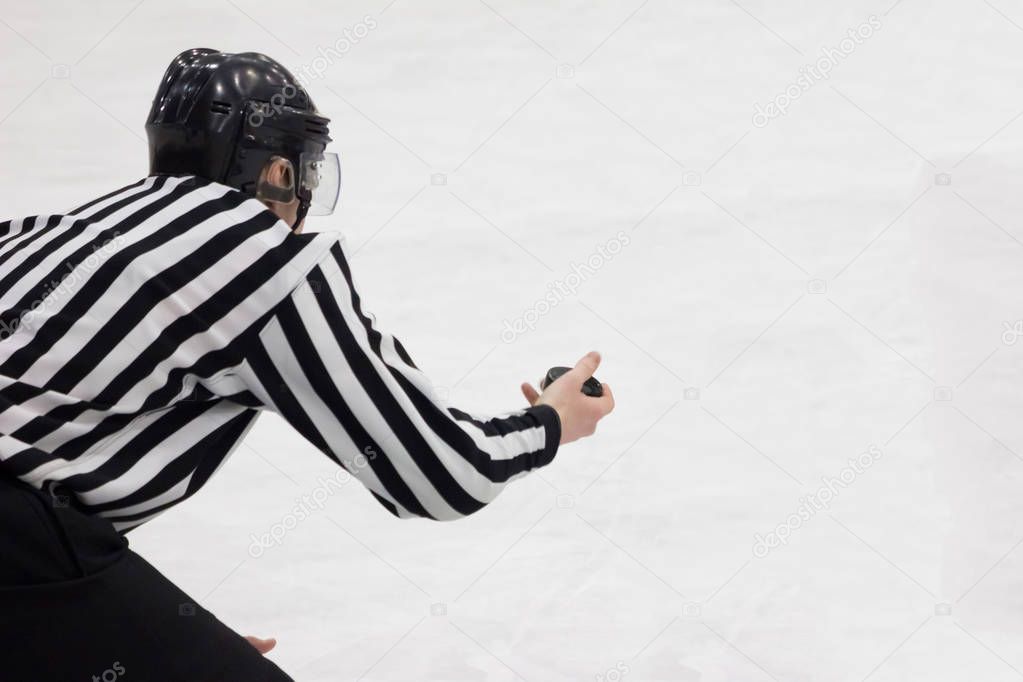 Hockey referee holding a puck in face off position. Back view. W
