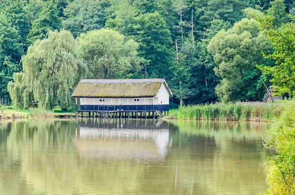 Casa costruita su acqua, tetto di paglia, vicino lago e foresta verde . — Foto Stock