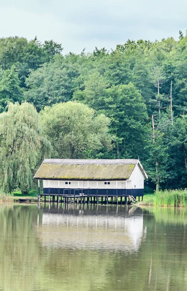 Casa costruita su acqua, tetto di paglia, vicino lago e foresta verde . — Foto Stock