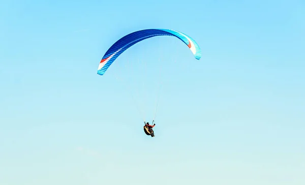 Man paragliding with blue parachute above water sea, clear sky — Stock Photo, Image