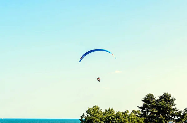 Man paragliding with blue parachute above water sea, clear sky — Stock Photo, Image