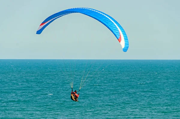 Homem parapente com paraquedas azuis acima do mar de água, céu limpo — Fotografia de Stock