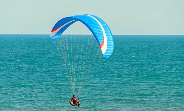 Man paragliding with blue parachute above water sea, clear sky — Stock Photo, Image