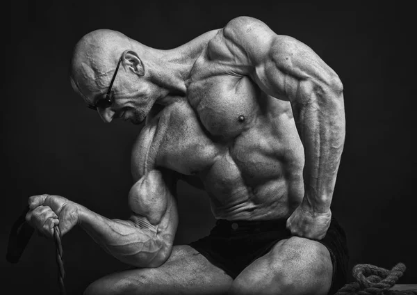 Brutala professionell bodybuilder sitter och poserar med motstånd band — Stockfoto