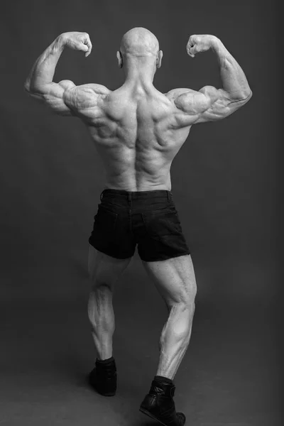 Athlète dans le dos pose double biceps. Bodybuilder montrant les muscles sur fond de studio gris — Photo