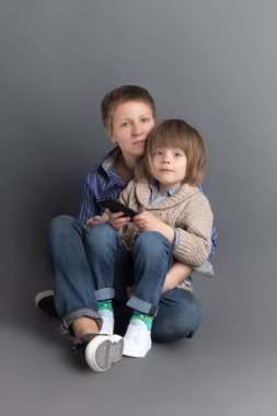 Mutlu anne ve 4 yaşındaki küçük oğlu birlikte oturan gri arka plan üzerinde studio için kot giymiş yıllarını ateş