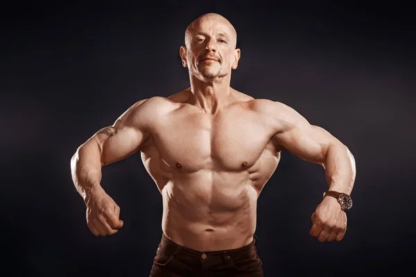 Bodybuilder posing on dark background in studio — ストック写真