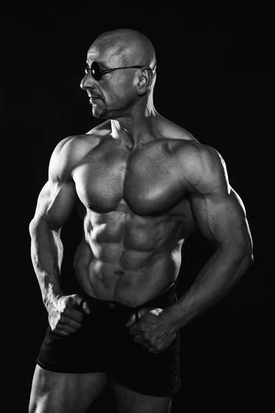 Portrait noir et blanc de bodybuilder chauve portant des shorts et des lunettes de soleil avec six pack parfait . — Photo