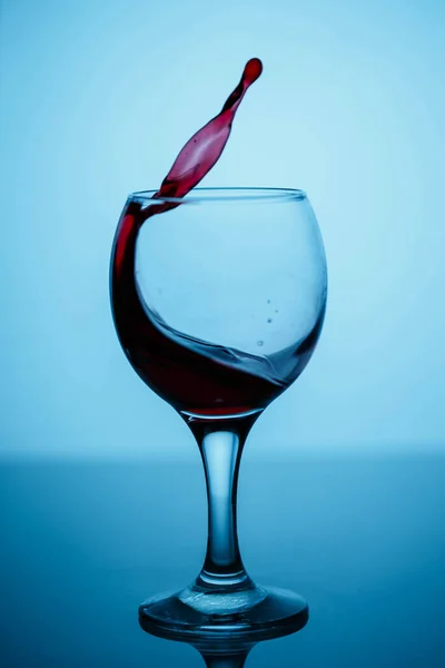 Salpicos de vinho tinto em um copo em um vidro brilhante preto em um blu — Fotografia de Stock