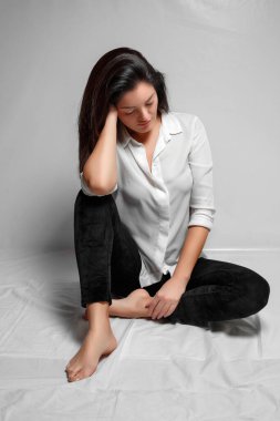 Beyaz gömlekli, siyah taytlı esmer bir kadın bir W 'nin üzerinde oturuyor.