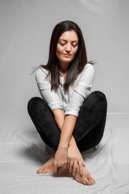 Beyaz gömlekli, siyah taytlı esmer bir kadın bir W 'nin üzerinde oturuyor.