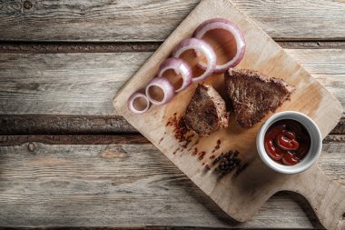 Baharatlı ızgara et ve aşınmış ahşap bir sırt üzerinde domates sosu.