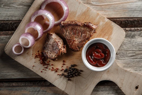 Grillat kött med kryddor och tomatsås på en sliten träbakdel — Stockfoto