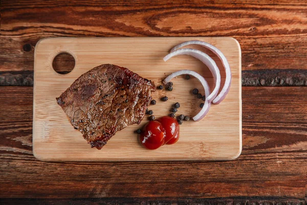 Gegrilltes Fleisch mit Gewürzen und Tomatensauce auf einem abgewetzten Holzrücken — Stockfoto