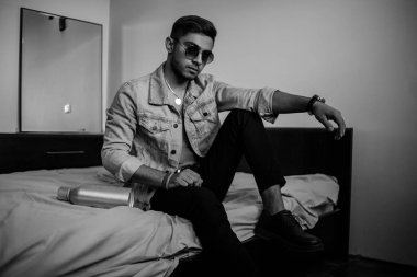 Kot ceketli, genç, şık bir adam yatağında bir şişe O ile.