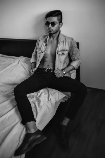 ベッドの上のデニムジャケットの若いスタイリッシュな男。黒と白のph — ストック写真