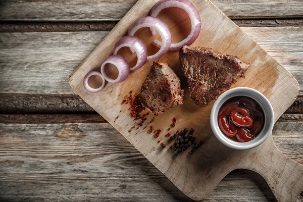 Grillat kött med kryddor och tomatsås på en sliten träbakdel — Stockfoto