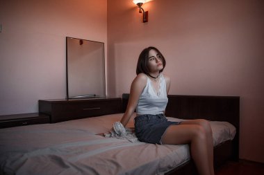 Mini etekli ve beyaz bluzlu genç bir kız yatakta oturuyor.