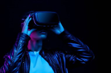 Genç Afro-Amerikalı kız VR gözlükleri kullanarak oyun oynuyor, oyun için 360 derecelik sanal gerçeklik kulaklığının tadını çıkarıyor, neon ışıklı siyah arka planda izole edilmiş.