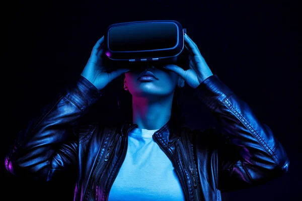 Siyah arka planda izole edilmiş, neon ışıklarla aydınlatılmış, sanal gerçeklik kulaklığıyla 360 derecelik video izleyen, VR gözlüklü Afrikalı Amerikalı kız.