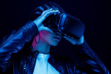 VR gözlüklü Afro-Amerikalı genç bir kadın 360 derecelik video izliyor. Sanal gerçeklik kulaklığı, neon ışıklı siyah bir arka planda izole edilmiş.