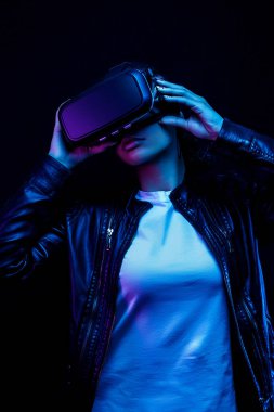 Genç Afro-Amerikalı kız VR gözlükleri kullanarak oyun oynuyor, oyun için 360 derecelik sanal gerçeklik kulaklığının tadını çıkarıyor, neon ışıklı siyah arka planda izole edilmiş.