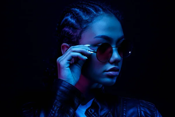 Moda joven mujer africana niña sostienen elegantes gafas de color rosa mirando a la cámara aislada sobre un fondo de estudio negro, pancarta horizontal para el diseño del sitio web, retrato, espacio de copia — Foto de Stock