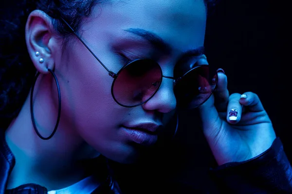 Moda joven mujer africana niña sostienen elegantes gafas de color rosa mirando a la cámara aislada sobre un fondo de estudio negro, pancarta horizontal para el diseño del sitio web, retrato, espacio de copia — Foto de Stock