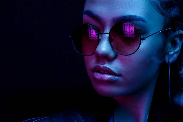 Porträtt av en afroamerikansk ung kvinna i solglasögon isolerad på en svart bakgrund i neonljus — Stockfoto