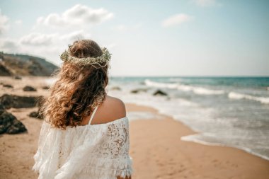 a bride in a white wedding dress on the beach with a wreath of flowers on her head. view from the back