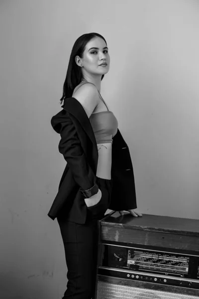 A beautiful Caucasian young woman in a black pantsuit and beige top poses next to a vintage record player — ストック写真