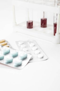Paketlerdeki ilaçlar ve arka plandaki test tüplerindeki kan örnekleri. beyaz bir tıbbi altyapıda