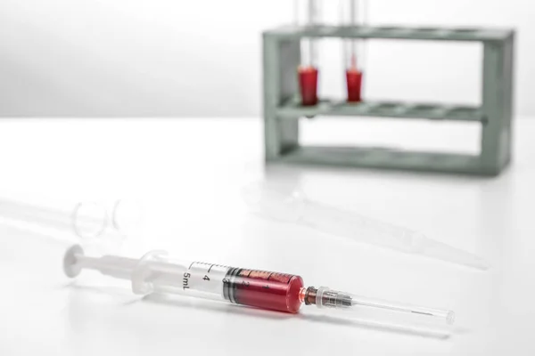Una jeringa estéril con una muestra de sangre sobre una mesa médica blanca. enfoque selectivo y área de enfoque pequeña — Foto de Stock