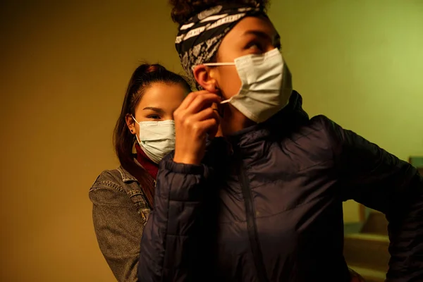 Молодая азиатская и африканская девушка в одноразовых медицинских защитных масках прячется от людей, зараженных вирусом на лестнице. спасение от вирусной инфекции. межрасовая международная помощь, fr — стоковое фото