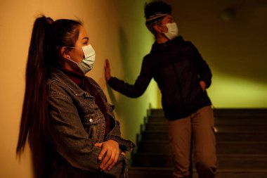 a young Asian and African girl in disposable medical protective masks is hiding from people infected with the virus on stairwell . rescue from virus infection. interracial international assistance, fr