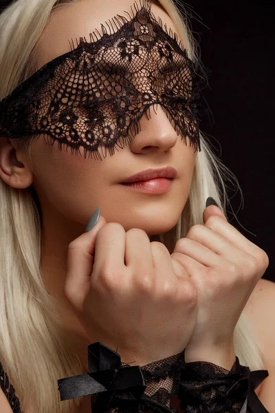 Retrato de una joven hermosa mujer rubia en una máscara de encaje y esposas de encaje sobre un fondo negro aislado — Foto de Stock